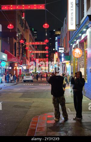 A young man and young woman taking photographs in Chinatown in Little Bourke Street at night in the Melbourne CBD, Victoria, Australia. Stock Photo