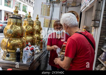 An assistant serves a customer with Freshly made Chinese tea from one of a set of traditional  Chinese brass tea dispensers  in Smith Street, Chinatown Stock Photo