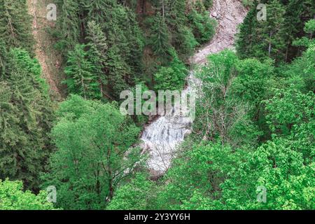 Waterfall is flowing down a hillside in a lush green forest.  Picturesque waterfall flowing gently in a tranquil woodland framed by rich greenery and Stock Photo