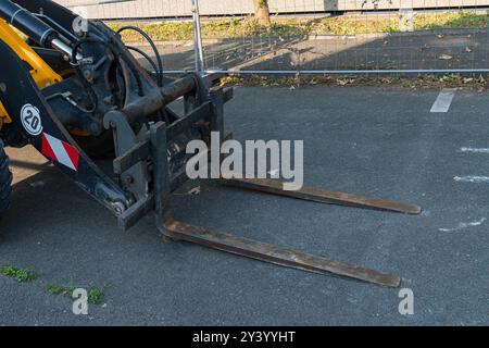 A forklift stands idle on a construction site, showcasing its extended forks. The area is marked by temporary fencing, with a clean asphalt surface an Stock Photo