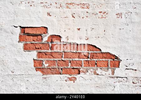 Texture of an old brick wall with damaged plaster and cracked white paint. Abstract background. Stock Photo