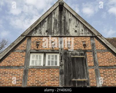 Close-up of a rustic half-timbered and brick gable with two small windows under a cloudy sky, heek, nienborg, muensterland, germany Stock Photo