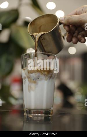 Freshly brewed espresso being poured over cold milk and ice, creating a beautiful layered coffee drink. Stock Photo