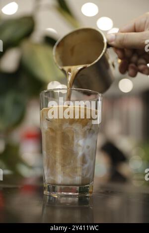 Freshly brewed espresso being poured over cold milk and ice, creating a beautiful layered coffee drink. Stock Photo