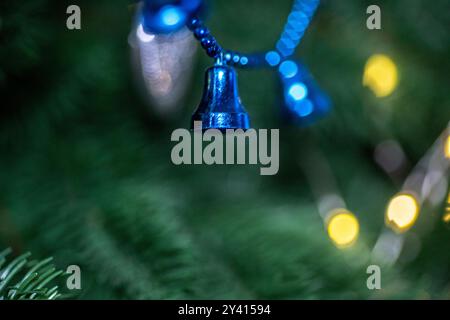 Bright blue bells are delicately hanging on a Christmas tree amidst lush green needles, creating a festive atmosphere enhanced by warm, glowing lights Stock Photo