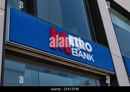 A close-up view of a Metro Bank sign on a modern building facade, showcasing the bank's logo in red and blue colors against a glass background. Stock Photo