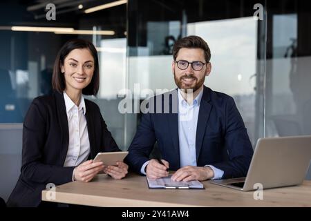 Business professionals collaborating on digital tablet and documents in modern office. Man and woman engaged in project discussion, showcasing teamwork and leadership skills with technology Stock Photo