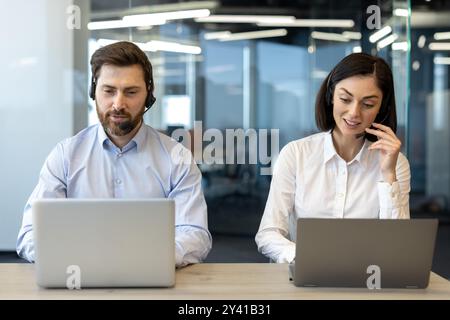 Focused customer service representatives use laptops in modern office. Professionals wearing headsets, engaged in communication and teamwork. Scene shows collaborative environment with technology Stock Photo