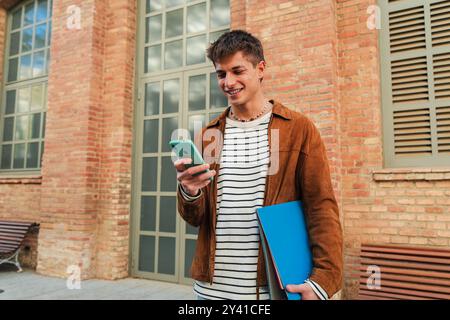 Horizontal portrait of a young Student Joyful Moment: A male student beams with a smile as he looks at his mobile phone, capturing a moment of happiness and connection in the midst of his studies. High quality photo Stock Photo