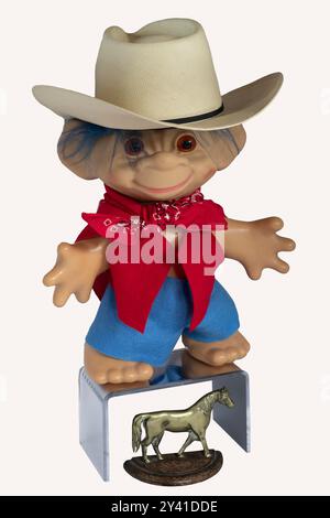 Little child troll with cowboy hat & red bandana stands with his toy dream horse below him. Young child plays while wearing his western costume. Stock Photo