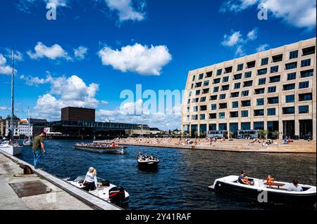 Copenhagen canals as seen from Christianshavn with  view of the Royal Danish Playhouse ( Skuespilhuset ) and people enjoying the sun on the waterfront Stock Photo