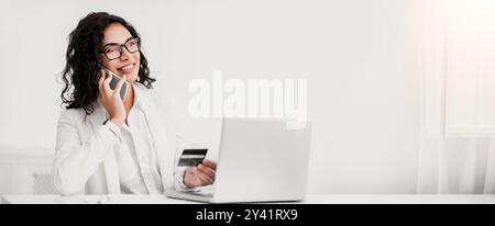 Latin woman holding credit card and talking on cellphone Stock Photo