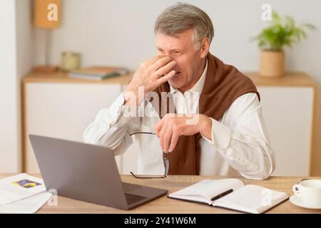 Elderly Businessman At Laptop Massaging Nosebridge Having Headache In Office Stock Photo