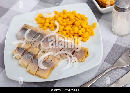 Sliced pickled herring fillet with corn and onions on plate Stock Photo