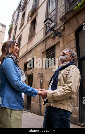 Smiling mature couple of cheerful retirees holding hands on city street. Happy adult love couple. Stock Photo