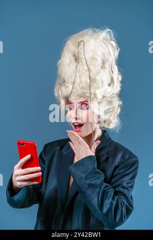 Royal online shopping. Funny princess, queen wearing vintage royal wig with red makeup woman using smart phone online shopping browses internet and networking in social media. Stock Photo