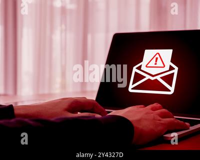 SMS spam, fake text message phishing scammer concept. Warning alert icon in opened envelope, e-mail hacked, scam malware spreading virus on laptop com Stock Photo