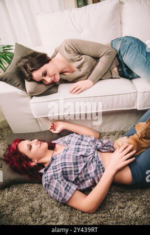 Two friends are lying down in their living room, taking a break from their day while their pet dog rests on the carpet with them Stock Photo