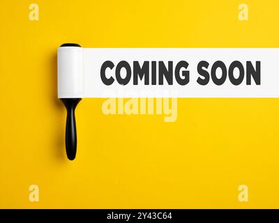 Coming soon announcement. Lint roller with white trace on yellow colored background with the announcement coming soon. Stock Photo