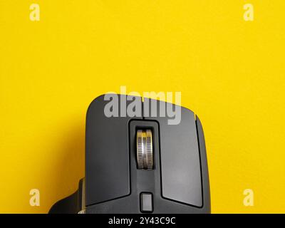 Black wireless computer mouse scroll wheel on yellow background. Close up top view with copy space. Stock Photo
