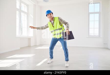 Young happy foreman working in empty new apartment wearing uniform and helmet. Stock Photo