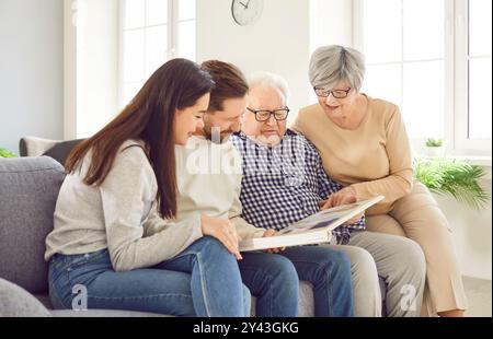 Happy family senior old parents adults daughter son sits together on sofa look family photo album. Happy family moment memories with photo album Stock Photo