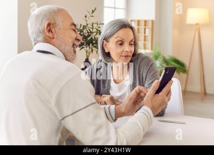 Senior couple sitting at the table in living room at home and using smartphone Stock Photo