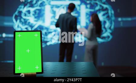 Green screen tablet used by computer scientists in startup doing advancements in AI field. Employees working on mockup device in workspace featuring artificial intelligence systems, camera B Stock Photo
