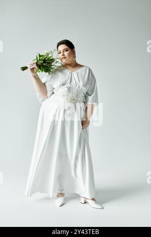 A stunning plus size bride elegantly poses in a white wedding dress with a bouquet, radiating bridal charm. Stock Photo