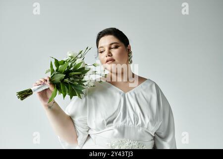 A stunning plus size bride elegantly holds a bouquet, radiating beauty and confidence against a grey background. Stock Photo