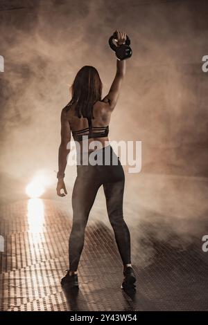 Empowered Fitness A determined woman confidently holding a kettlebell in a smokelit gym, radiating strength and focus, embodies the essence of hard Stock Photo