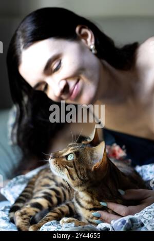 Bengal cat looks up while serene woman lovingly holds it Stock Photo