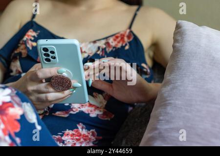 A woman in a floral dress using a smartphone, lounging on a sofa Stock Photo