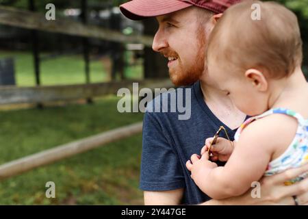 Father in red baseball hat holding infant daughter in the park Stock Photo