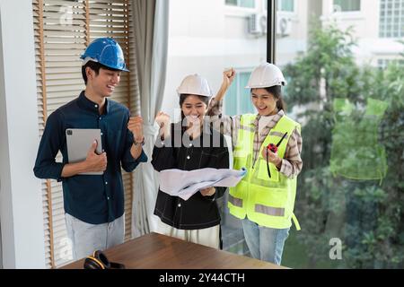 Group of Engineers Celebrating Success with Blueprints in Modern Office Setting Stock Photo
