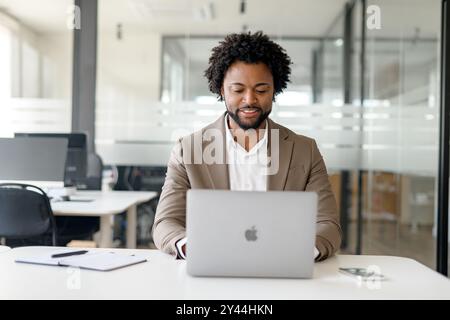 A proficient African-American businessman focuses on his laptop in a bright, contemporary office, signifying dedicated work ethic and modern entrepreneurial spirit Stock Photo