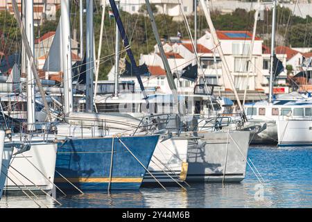 White sailing yachts are reflecting in the calm waters of adriatic sea with residential buildings in the background. Rogoznica, Croatia Stock Photo