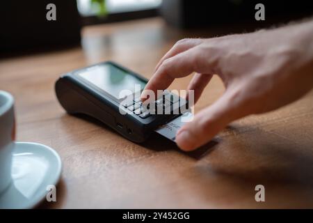 Man palm typing POS terminal buttons pin-code credit doing wireless bank payment with process acquire at table cafe restaurant indoor. Focus on machin Stock Photo
