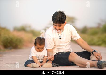 father and baby boy are sitting playing on the small grass. they wore white couple clothes. photo atmosphere in a sunny afternoon outdoors. Stock Photo