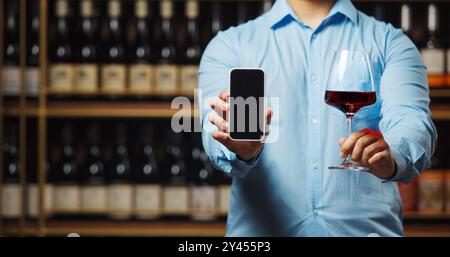 Close up Unrecognizable Person Holding Glass of Wine and Showing Screen Smartphone in Wine Shop. Stock Photo