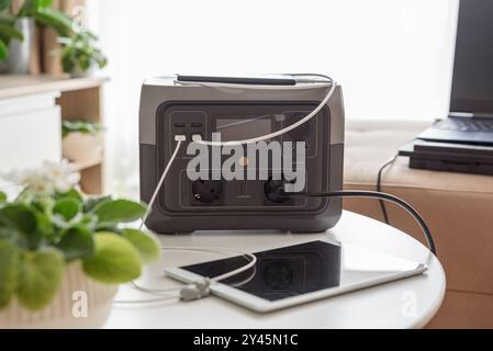 Uninterruptible power supply source. Workspace on sofa with laptop, tablet, smartphone and portable power station Stock Photo