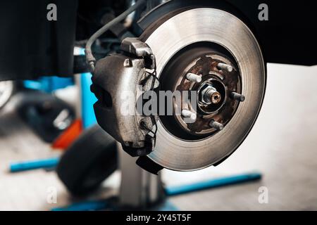 Close up of a car disk brake being repaired in a workshop, showing the brake caliper, rotor, and other components Stock Photo