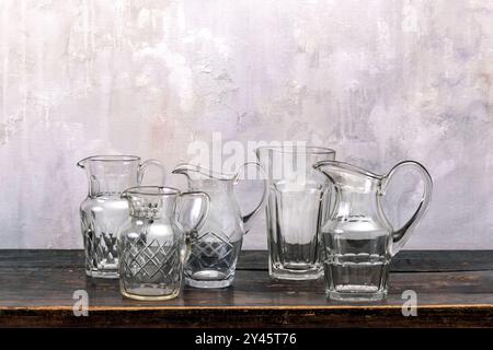 Set of transparent glass jugs placed on timber tabletop against shabby gray wall Stock Photo