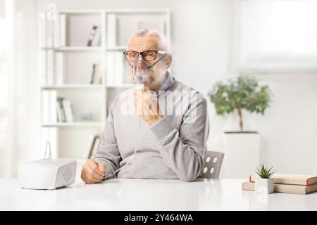 Senior man sitting at home and using a nebulizer with mist Stock Photo