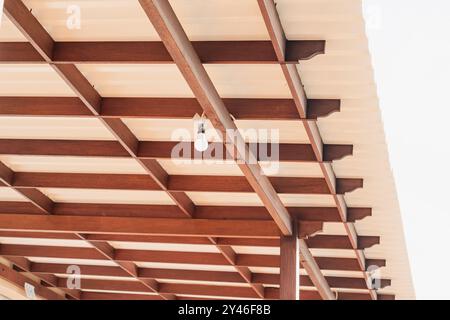 A close-up view of a wooden ceiling structure with exposed beams and a single light bulb hanging from it. The ceiling features a combination of wooden Stock Photo