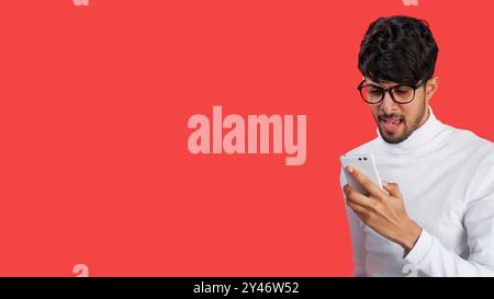 Mobile conflict. Online chat. Internet disagreement. Annoyed frustrated angry man yelling on phone isolated on red empty space background. Stock Photo
