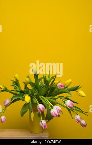 Bouquet of soft pink tulips in yellow vase on yellow background.  Copy space. . Postcard. Congratulations. Wishes. Still life. Stock Photo