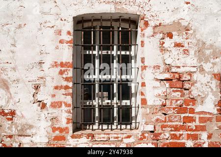 Barred window of an old prison on a white brick wall. Jail and imprisonment concept. Old damaged wall. Stock Photo