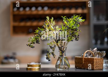A branch of blueberries with berries in a glass vase close up. A vase with blueberry branch in it. Bokeh background. Stock Photo