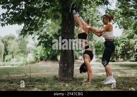 Women practicing outdoor workout together, doing handstand against tree in park Stock Photo